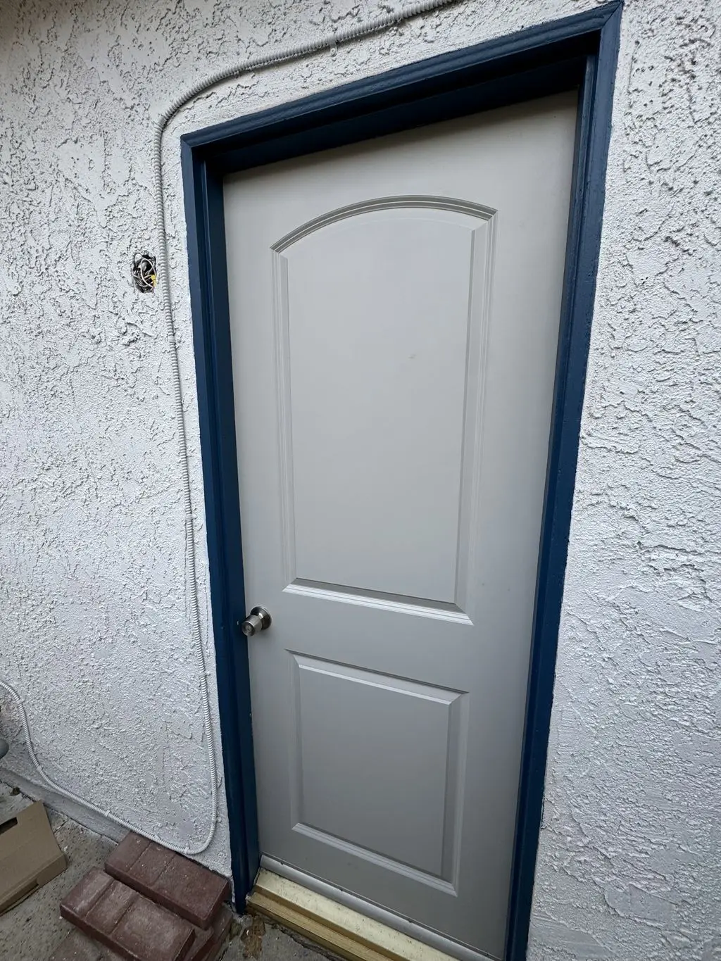 White arched panel door set in a stucco wall with a dark painted frame. Work by Construction Hub in Los Angeles.