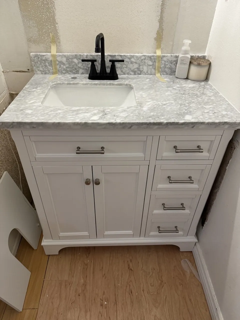 New white vanity with marble-look top and black faucet installed on wood-look floor. Work by Construction Hub in Los Angeles.
